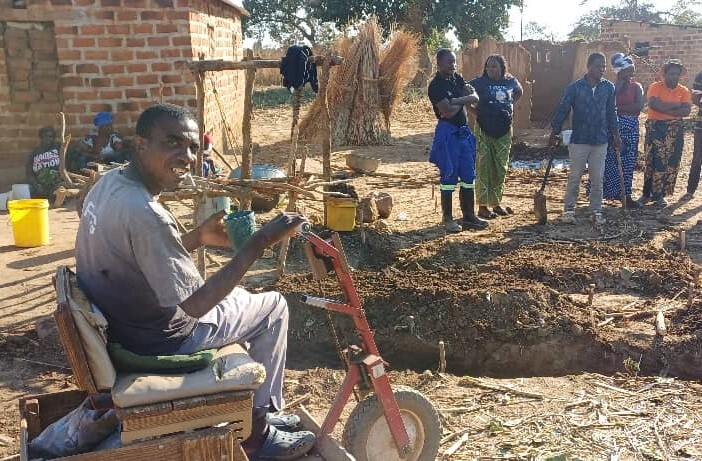 Man in wheelchair in front of water harvesting structure